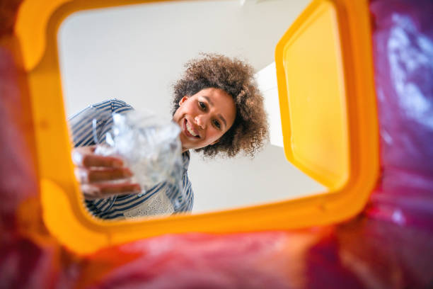 Mixed Race Mid Adult Woman Recycling Plastic Viewed From Inside Garbage Bin Mixed race mid adult woman are putting plastic into a garbage bin at home. She is recycling trash. Viewed from inside recycling bin. garbage bin photos stock pictures, royalty-free photos & images