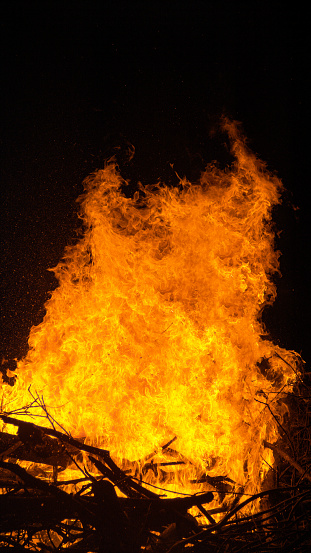 CLOSE UP, VERTICAL: Detailed shot of fiery hot flames engulfing a big pile of dry firewood near a beautiful campsite on a tranquil summer night. bonfire gets ignited in the dark of the fall night.