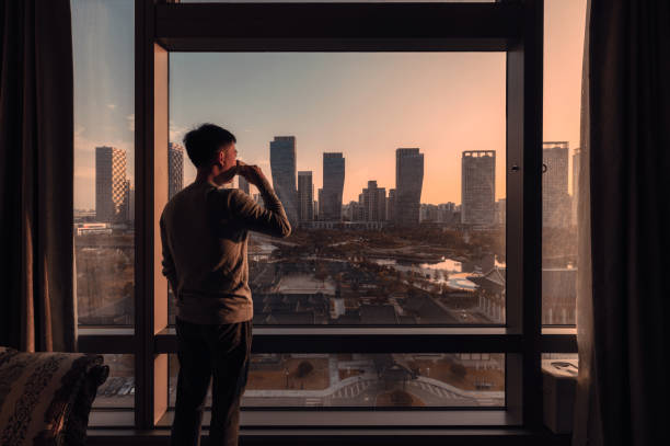 Young asian man standing with drinking coffee in a hotel. Sunrise over modern buildings in Songdo central park at Incheon Young asian man standing with drinking coffee in a hotel. Sunrise over modern buildings in Songdo central park at Incheon, South Korea songdo ibd stock pictures, royalty-free photos & images