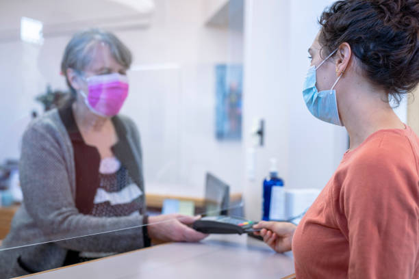 mujer de raza mixta paciente que paga factura médica en consultorio dental - healthcare and medicine receptionist paying credit card fotografías e imágenes de stock