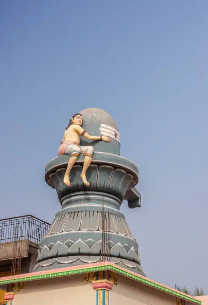 Hospet, Karnataka, India - November 10, 2013: Markandeshwara Temple top, closeup of decoration featuring giant Shivalingam with boy statue holding on to it. Blue sky.