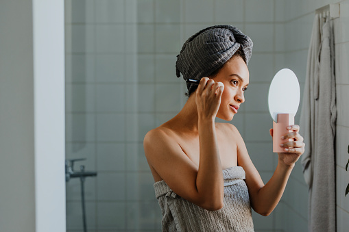 A good-looking young woman applying makeup in the morning after having a shower.
