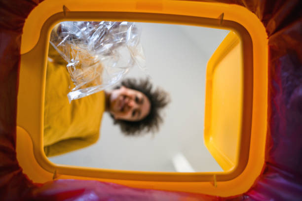 Mixed race teenage girl is putting plastic into a garbage bin at home. She is recycling trash. Viewed from inside recycling bin.