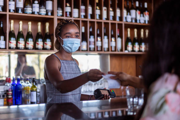 istock Waitress at bar collects payment from female customer using contactless payment 1303559806