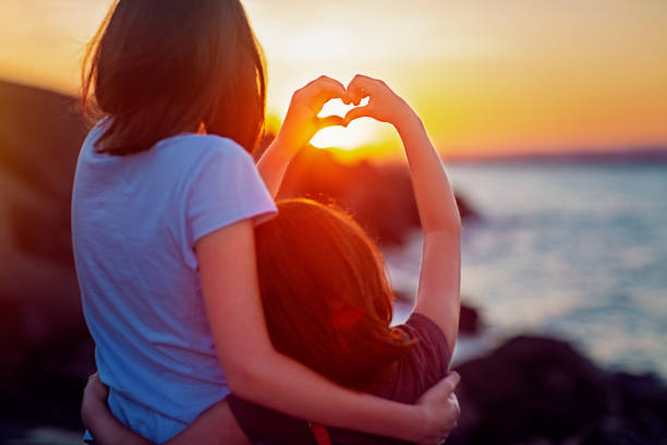 istock Girlfriends are doing heart with their hands and enjoying sunset 1303560584