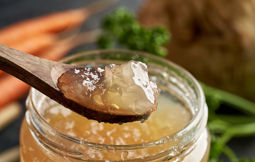 Cooled jellied beef bone broth on a spoon and in a glass jar