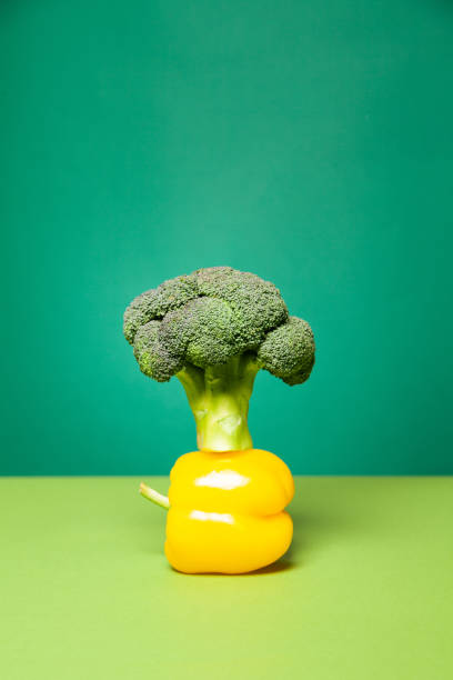 istock Ripe yellow bell pepper placed on broccoli head against green background 1303562257