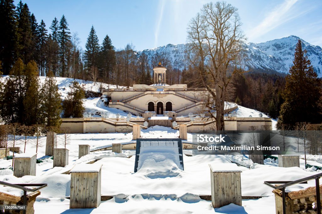 Linderhof Castle Palace in the German Snow covered alps on a sunny Winter Day in Bavaria. A popular Tourist Destination in the European Austrian Mountains. It's a fountain in the summer time and a winter wonderland in the cold season. Ancient Stock Photo