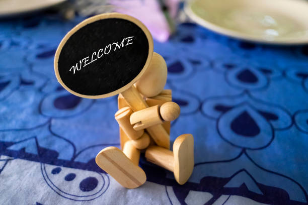 wooden dummy sitting on a restaurant table holding a welcome sign, selective focus on the text, horizontal