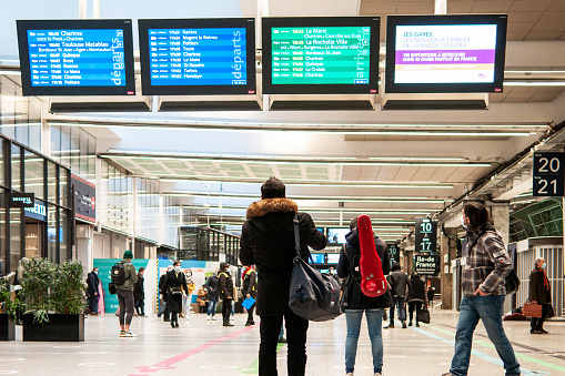 A train station during pandemic Covid 19, people in front of departure board. Gare Montparnasse in Paris, France. January 27, 2021.