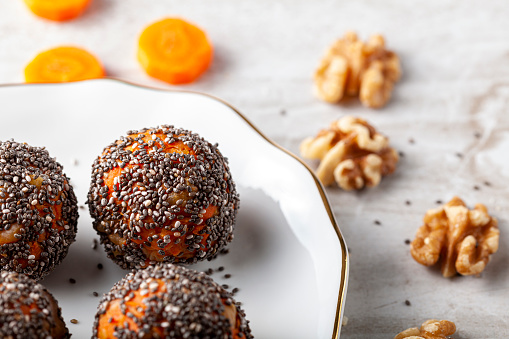 Angled view of kitchen countertop with a flat porcelain plate. Homemade fresh carrot bliss balls (mixture of cookie crumbles, walnut and carrot puree) coated with chia and poppy seeds are ready.
