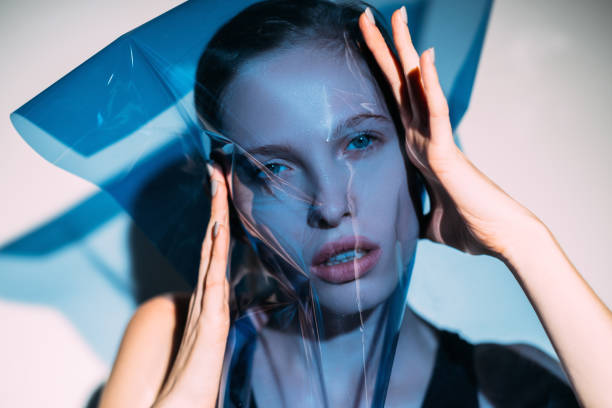 fashion art portrait female model face blue filter Fashion art portrait. Aesthetic cosmetology. Beauty enhancement. Sensual female model covering face with blue colored transparent wrinkled plastic filter in spotlight. vogue cover stock pictures, royalty-free photos & images