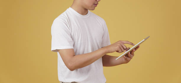 istock young asian man dressed casually using digital tablet isolated on yellow background. 1303582115