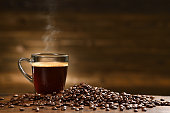 istock Cup glass of coffee with smoke and coffee beans on old wooden background 1303583671