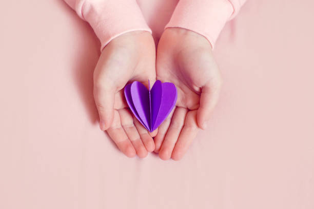 International world epilepsy illness awareness day. Kid girl hands holding small violet purple paper heart. Support, care and solidarity with illness struggle concept. Mental health medicine. stock photo
