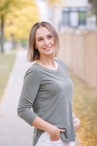 Beautiful middle age Caucasian woman with short hair walking in autumn fall street outdoors. Young woman with short haircut in casual clothes in park outside. Little memorable moments of life.
