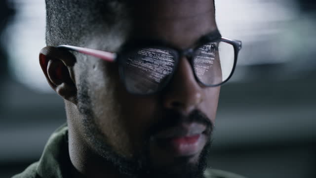 4k footage of a young male programer looking at his monitor with the screen reflecting on this glasses while working late at night