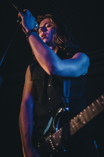 One man, guitarist playing electric guitar and singing in music bend, performing at rock concert on stage in night club.