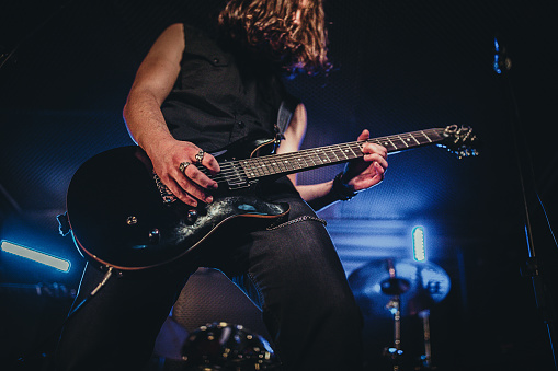 One man, guitarist playing electric guitar in music bend, performing at rock concert on stage in night club.