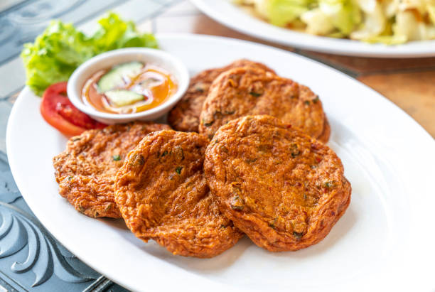 Tod Mun Pla or Curried fish cake of Thai food menu. Traditional Thai food deep-fried curried fish cake in white plate on table restaurant, natural light, close up food image.