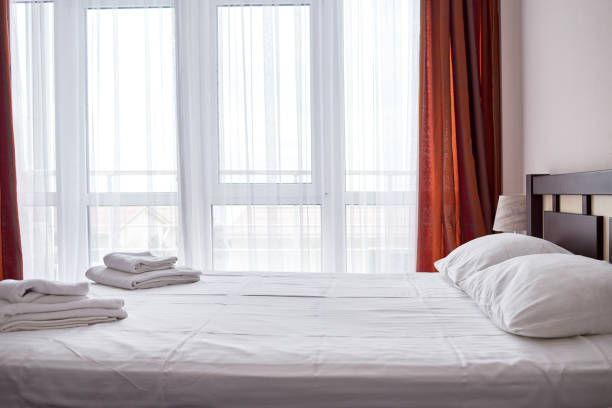 A bed with a white pillow and a pink blanket. There are four white towels on the bed