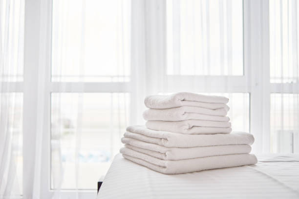 배경에 창문이있는 현대적인 호텔 침실 인테리어의 침대 시트에 신선한 흰색 목욕 수건 더미, 복사 공간 - textile folded white nobody 뉴스 사진 이미지
