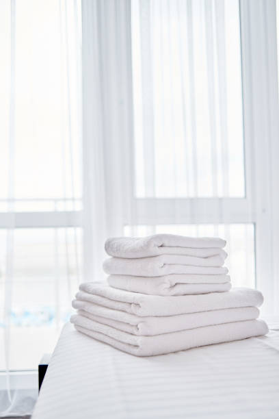 Woman in towel in bedroom opening curtain on bright day
