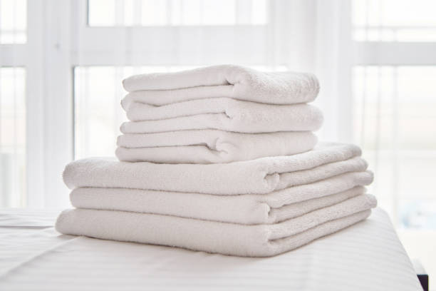 istock Stack of white clean bath towels on bed sheet in modern bedroom interior, copy space. Close up 1303589713