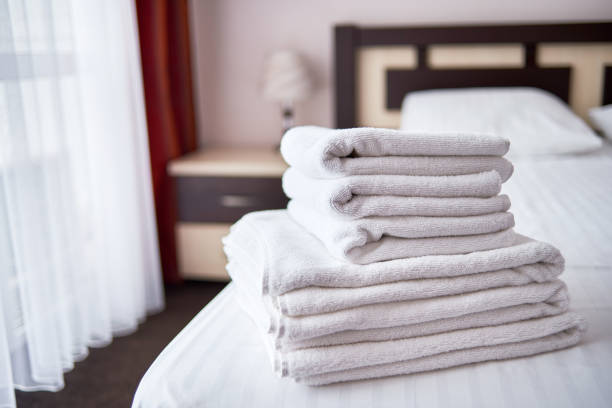 istock Stack of white clean bath towels on bed sheet in modern hotel bedroom interior, copy space 1303589722