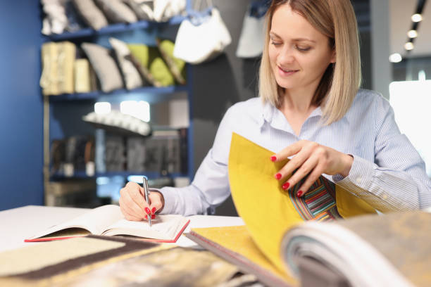 istock Woman writing with pen in notebook and leafing through catalog with fabrics 1303589871