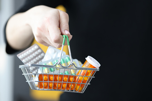 Womans hand holding basket with blisters of pills closeup. Sale of medicines concept