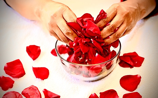 Woman of color massages red rose petals in and around a glass bowl.