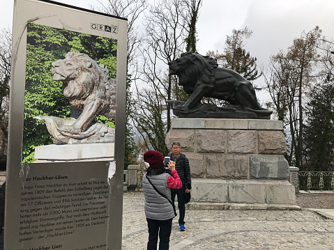 Graz, Austria - November 9, 2018:  An asian couple is taking a photo with the Hackher Lion statue at the Schlossberg park in Graz, Austria.