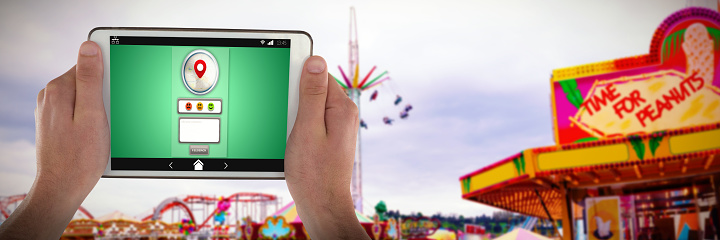 Hands holding digital tablet against fairground ride in amusement park