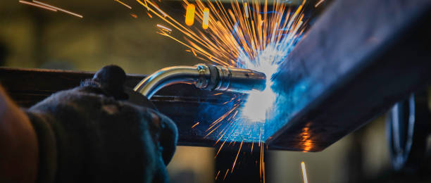 industrial welder with torch in big hall welding metal profiles - soldar imagens e fotografias de stock