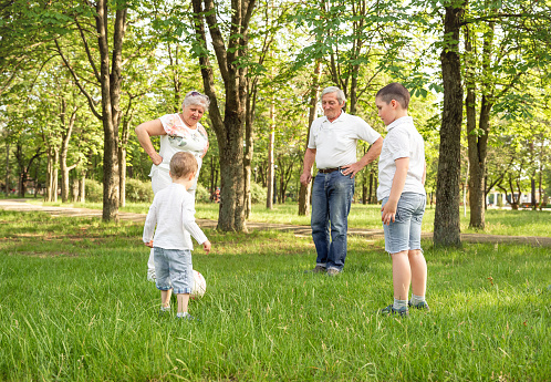 Grandparents with his little cute grandchildren are having fun and playing football on green grassy lawn. Happy family playing soccer on summer meadow. Active family play soccer in their leisure time