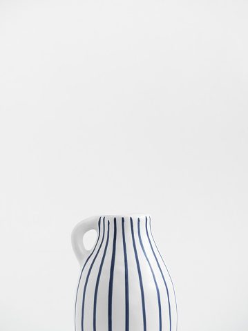 White ceramic jug with blue stripes isolated on white background. Trend minimalistic composition. Boho or Scandinavian style poster in modern home interior. Copy space. Close-up.
