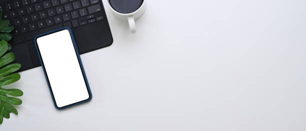 Horizontal image of modern office desk with smart phone, coffee cup, wireless keyboard and copy space on white background.