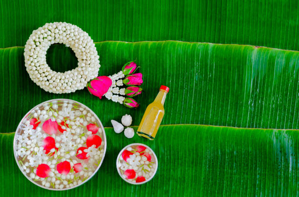 Songkran festival background with jasmine garland, flowers in water bowls, scented water and marly limestone for blessing on wet banana leaf background.
