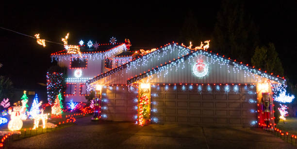 Crawley, UK - 18 December, 2021: a terraced house decorated with fairy lights and festive inflatables, including snowmen and a santa claus, in the front garden for Christmas on a residential street at night.
