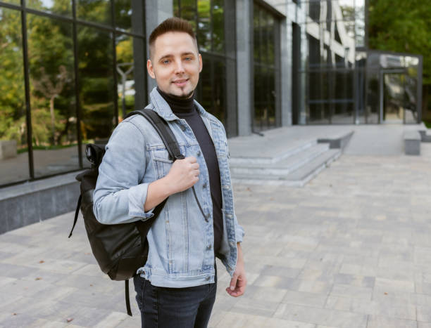 istock Modern young student man in stylish denim jacket and backpack outdoors 1303618560