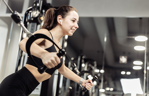 Young fit woman trains pectoral misci in a crossover exercise machine. Girl works out in modern gym