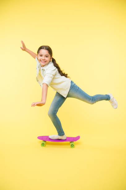 istock Kid having fun with penny board. Hobby favorite activity. Child smiling face stand on skateboard. Penny board cute colorful skateboard for girls. Lets ride. Girl ride penny board yellow background 1303624411