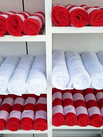 Stacks of rolledup red and white towels in a cabinet.