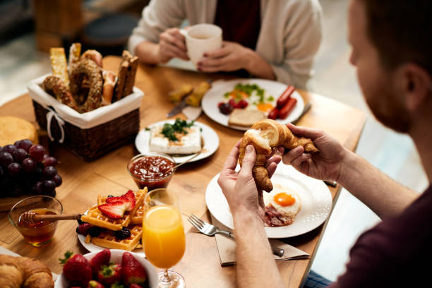 istock Close-up of man having croissant for breakfast at dining table. 1303625333