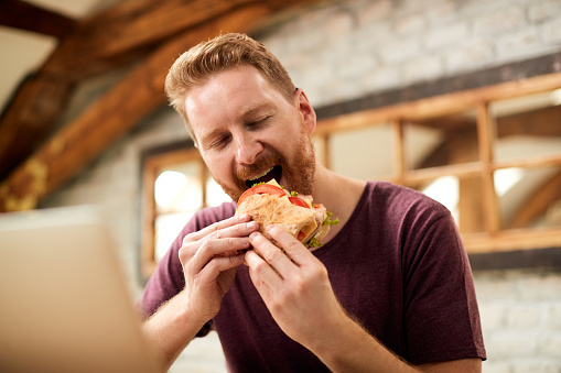 Man with eyes closed eating sandwich for breakfast at home.