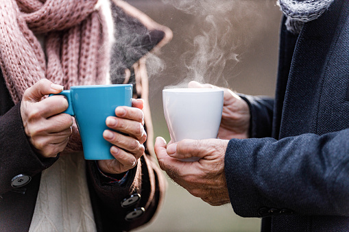 Close up of unrecognizable mature couple holding mugs with hot drinks in nature.