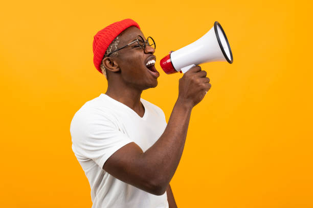 istock black african man speaks in megaphone on isolated yellow background 1303629260