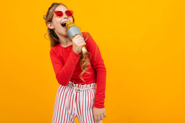 istock young singer comes off to music with a microphone in her hands on a yellow studio background with copy space 1303630569