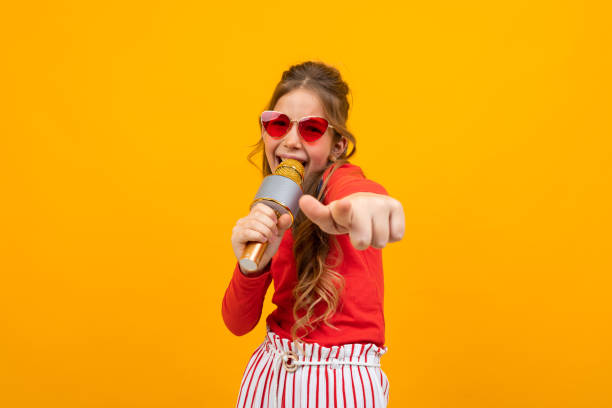 young singer comes off to music with a microphone in her hands on a yellow studio background with copy space